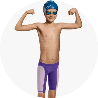 Young swimmer wearing a blue swim cap, goggles, and purple swim jammers flexing muscles. Ideal swimwear for competitive youth swimmers.