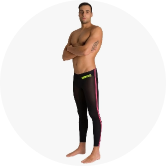 Man wearing black swimming jammers with pink side stripes, standing with arms crossed. The swimwear features a yellow waistband logo, suitable for competitive swimming.